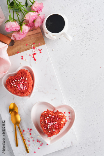 Two cakes Red velvet in shape of hearts on white plate, rose flowers and cup of coffeeon on pink romantic background. Dessert idea for Valentines Day, Mothers or Womens Day. Tasty homemade dessert. photo