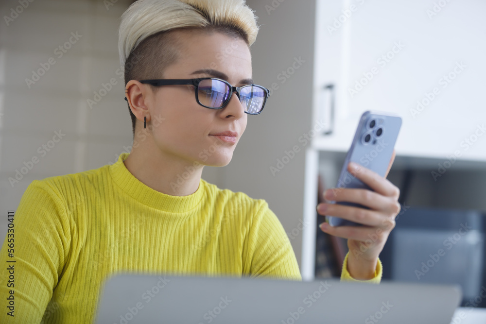 Portrait of stylish young woman with short blond hair browsing mobile app on smart phone. Freelancer person networking online with customers
