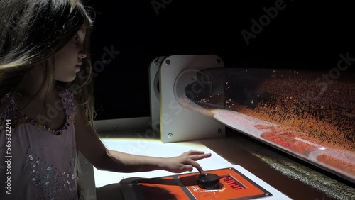 Junior schoolgirl examines acoustical device. Kid changes sound frequency and observes foam plastic particles in tube against black background closeup photo