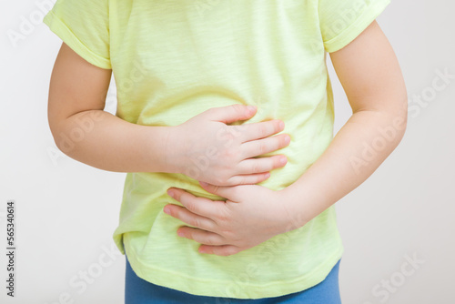 Little girl touching painful belly with arms isolated on light gray background. Closeup. Front view. Child suffering from stomach ache.