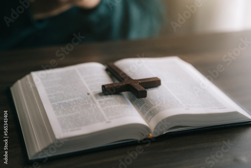 Close up of an open bible with a cross for morning devotion on a wooden table with window lights.