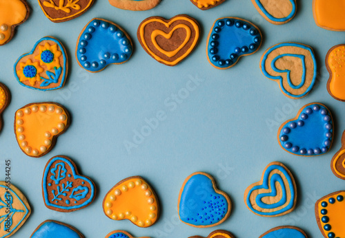 Valentine’s day composition with cookies in shape of hearts decorated by yellow and blue icing and sprinkles on blue background
