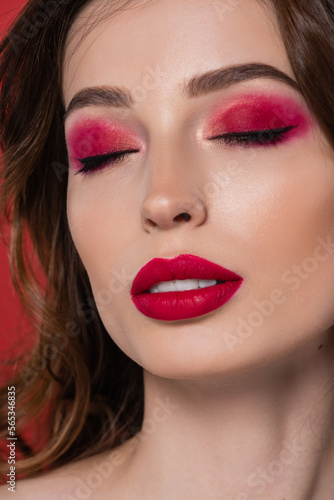 close up of young woman with closed eyes and magenta color eye shadow isolated on pink.