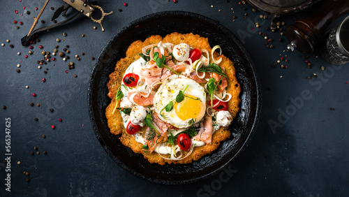 Large potato pancake with salmon fish, tomatoes, egg, onion, herbs and sour cream in a frying pan.