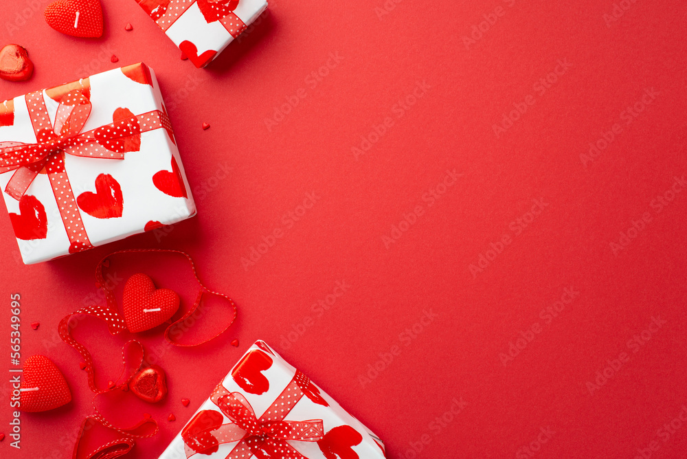 Valentine's Day concept. Top view photo of present boxes with ribbon bows heart shaped candles chocolate candies and sprinkles on isolated red background with copyspace Valentine's Day concept. Top view photo of present boxes with ribbon bows heart shaped candles chocolate candies and sprinkles on isolated red background with copyspace