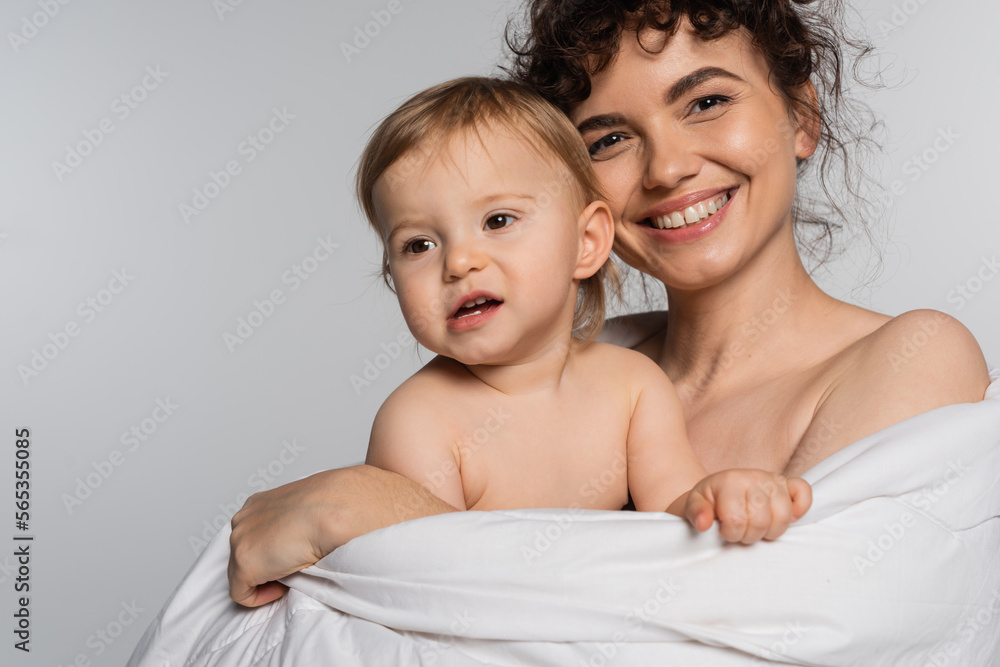 smiling mother and toddler baby girl covered in duvet isolated on grey. smiling mother and toddler baby girl covered in duvet isolated on grey.