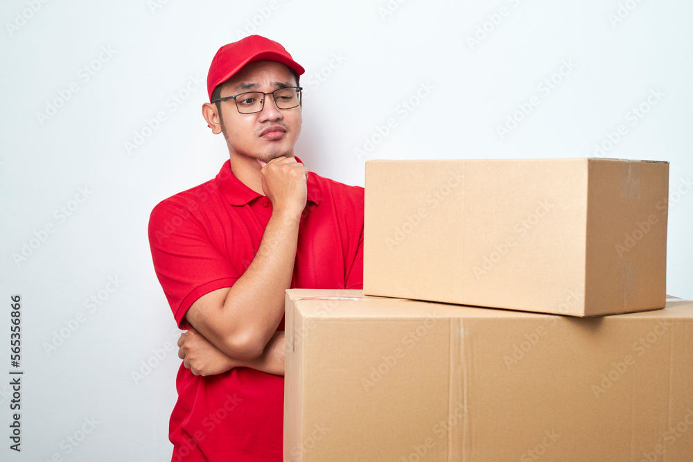 Concerned and troubled asian courier in red uniform and cap grab head and gasping shocked staring at cardboard boxes Concerned and troubled asian courier in red uniform and cap grab head and gasping shocked staring at cardboard boxes