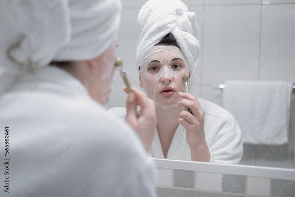 Beautiful young woman doing facial massage with gua sha tool in front of mirror at home Beautiful young woman doing facial massage with gua sha tool in front of mirror at home