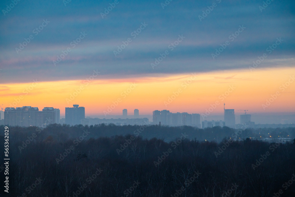 early winter cold dawn over dark city park and houses on horizon