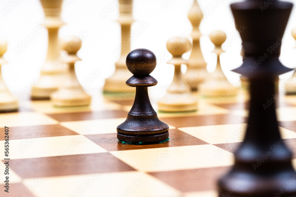 attacking black pawn and queen against white chess pieces in background on wooden chessboard close up (focus on the black pawn) attacking black pawn and queen against white chess pieces in background on wooden chessboard close up (focus on the black pawn)