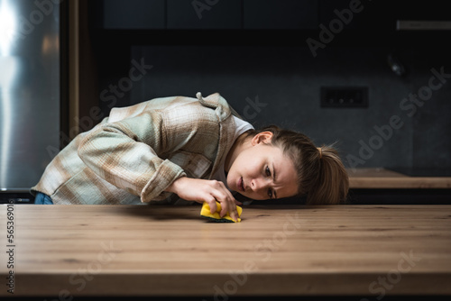 Young woman suffers from depression after a breakup or divorce and from obsessive compulsive disorder OCD cleans kitchen cook top to calm her nerves. Serious stressed female rubbing the home photo