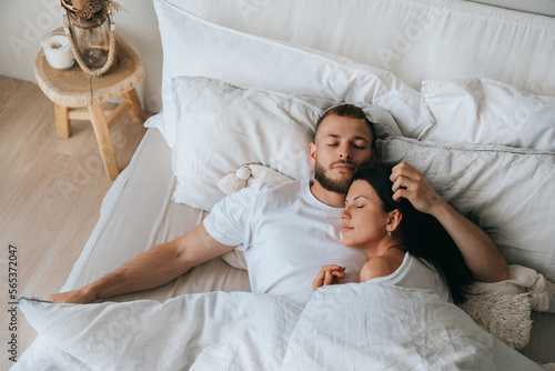 Young caucasian sleeping couple in bed. Handsome beardy European man laying with wife at bedroom enjoying Sunday morning. Calm hispanic young adult woman having nap at hotel with husband.