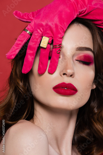 brunette young woman in magenta color glove with golden rings covering eye isolated on pink.