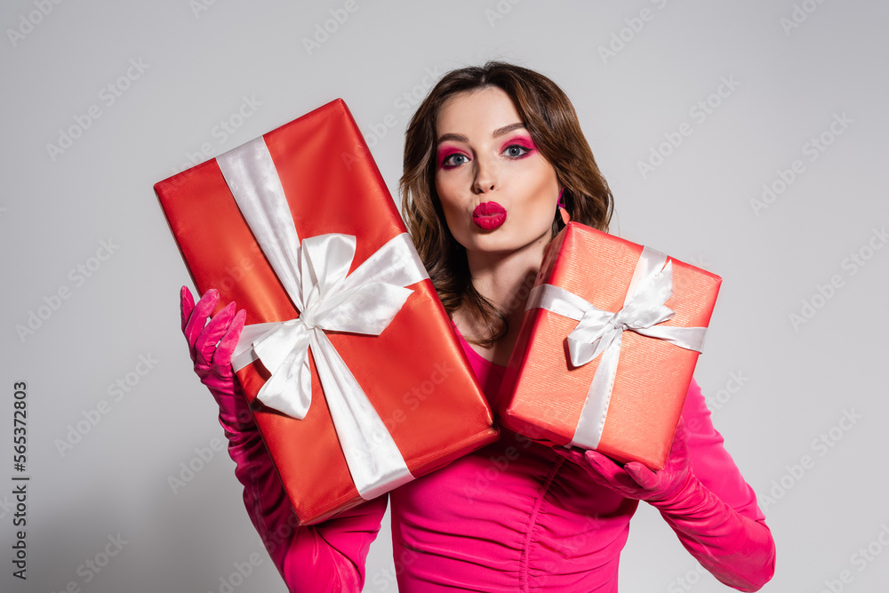 brunette young woman in magenta color gloves holding presents while pouting lips isolated on grey. brunette young woman in magenta color gloves holding presents while pouting lips isolated on grey.