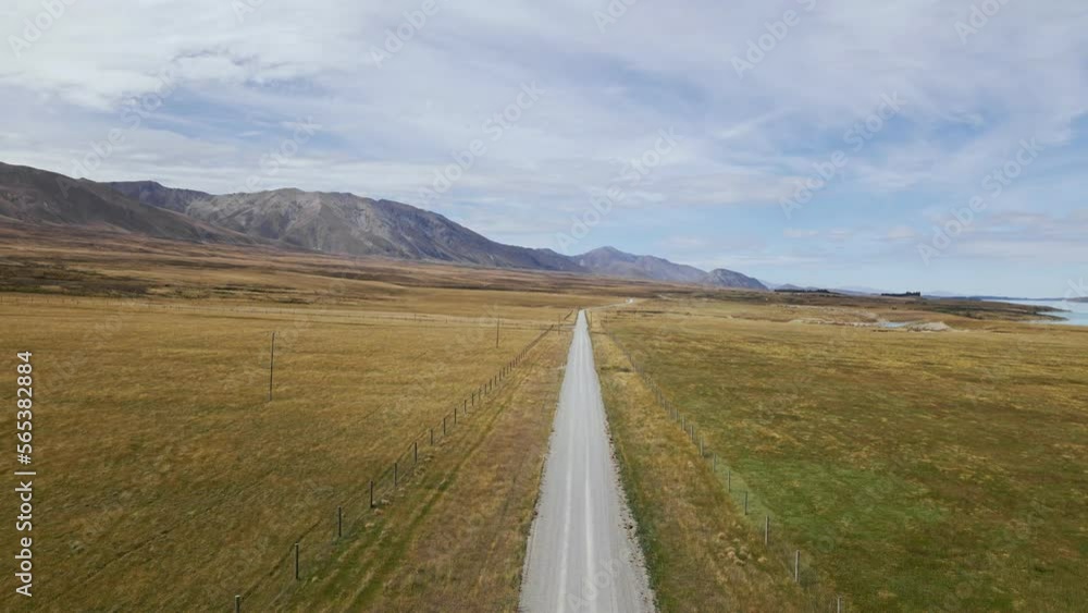 A vehicle navigating a dusty, unpaved road through a barren, mountainous landscape with a lake visible in the distance on a sunny day A vehicle navigating a dusty, unpaved road through a barren, mountainous landscape with a lake visible in the distance on a sunny day