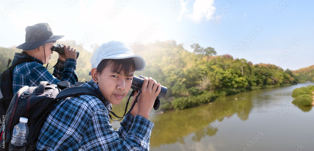 Asian boys are using binoculars to do the birdwatching in tropical forest during summer camp, idea for learning creatures and wildlife animals and insects outside the classroom.