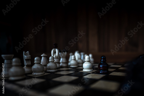 Blurred background with a low depth of focus. The set of wooden chess pieces elements standing on chess board on dark background.