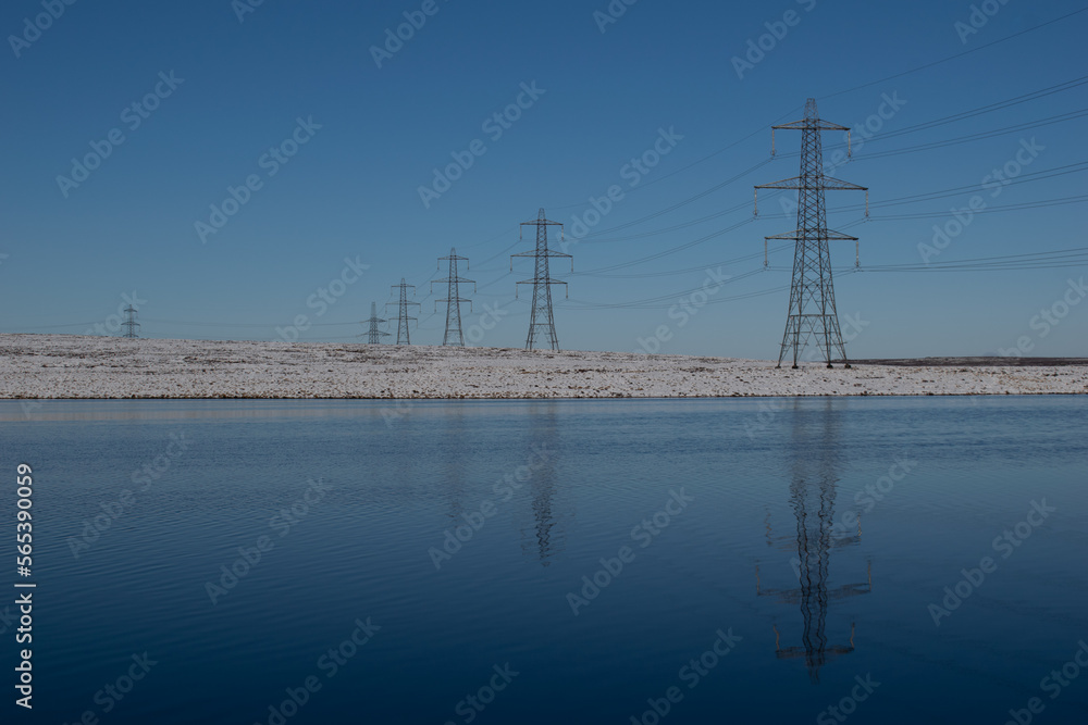 Electricity pylons reflected in water with covering of snow 