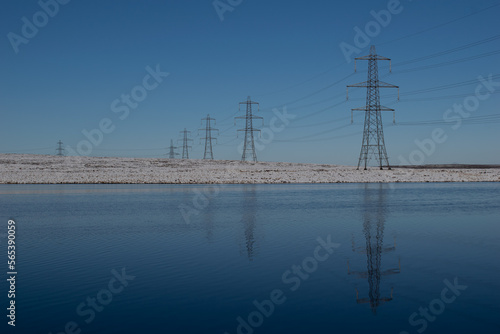 Electricity pylons reflected in water with covering of snow 