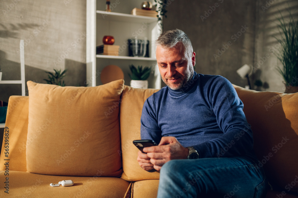Middle aged man using smartphone while sitting on a sofa at home