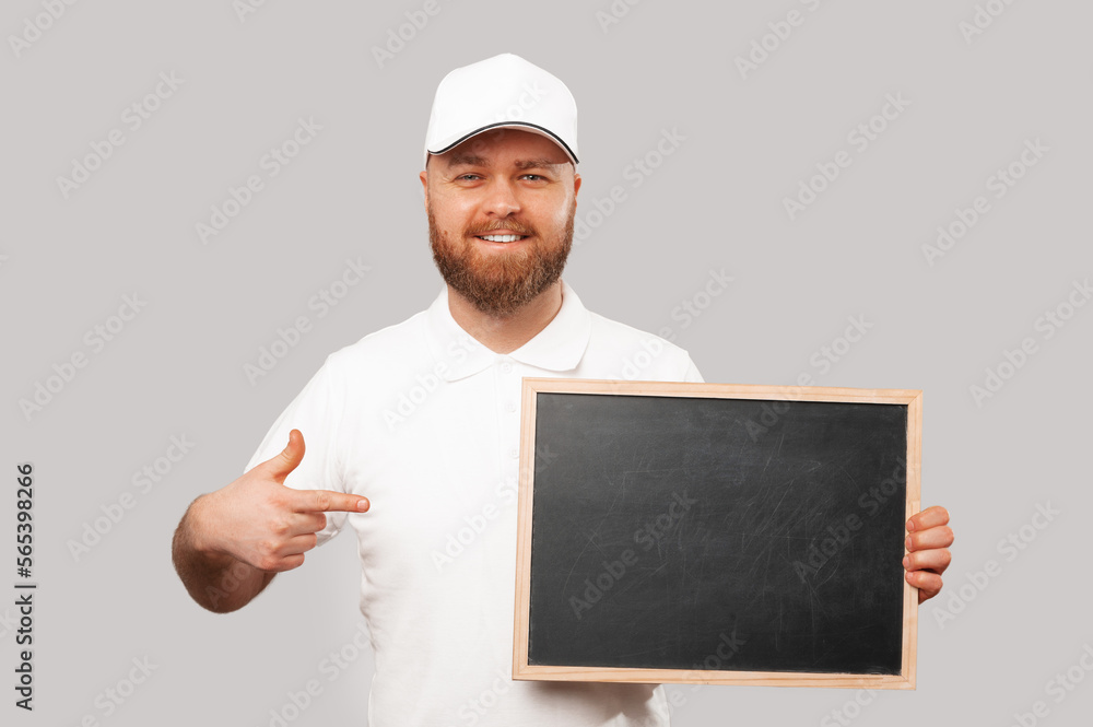 Cheerful bearded man wearing white is pointing at the blackboard he is holding. Cheerful bearded man wearing white is pointing at the blackboard he is holding.