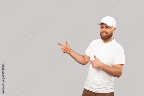 Bearded man wearing white cap and t shirt points aside at the grey copy space. photo