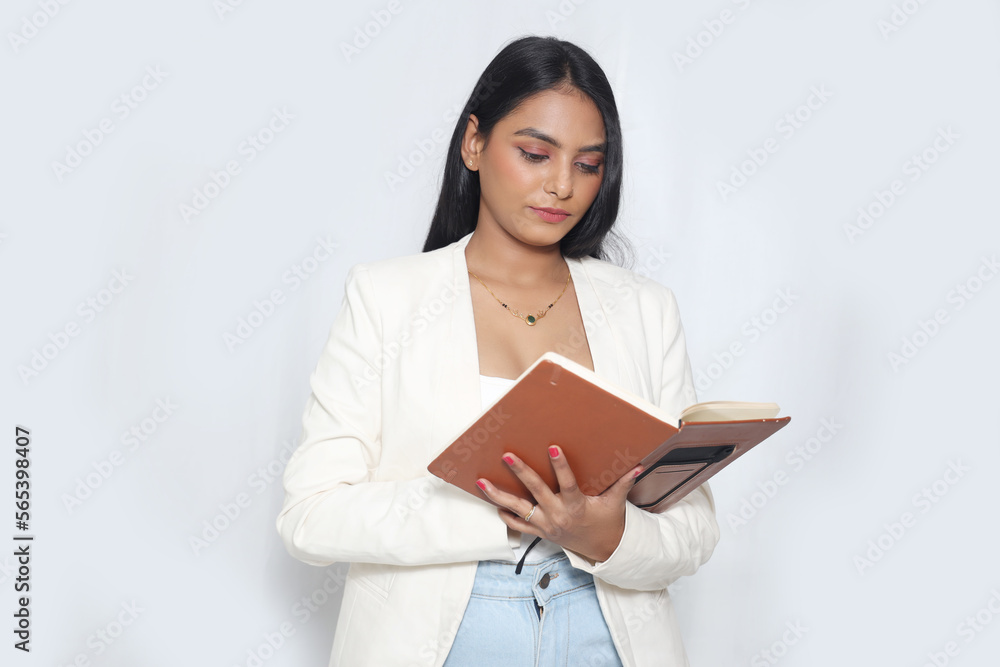 Writing notes in notebook. Beautiful young Indian business woman in white Blazer isolated on gray background studio portrait. Mock up copy space. Writing notes in notebook. Beautiful young Indian business woman in white Blazer isolated on gray background studio portrait. Mock up copy space.