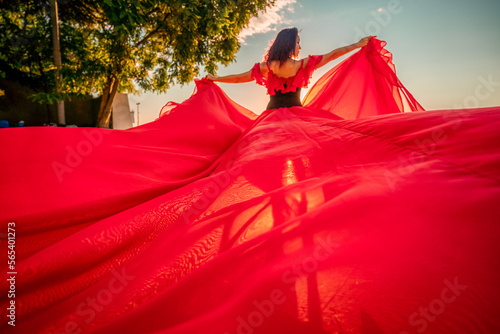 Sunrise red dress. A woman in a long red dress against the backdrop of sunrise  bright golden light of the sun s rays. The concept of femininity  harmony.