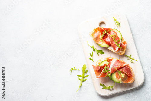 Open sandwiches with cream cheese, prosciutto and arugula at white background. Top view with copy space.