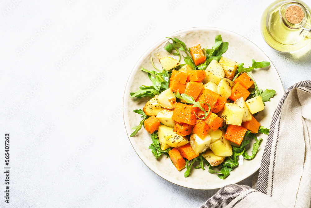 Pumpkin salad. Warm baked pumpkin, potato with spices and fresh arugula. Top view on white with copy space. Pumpkin salad. Warm baked pumpkin, potato with spices and fresh arugula. Top view on white with copy space.