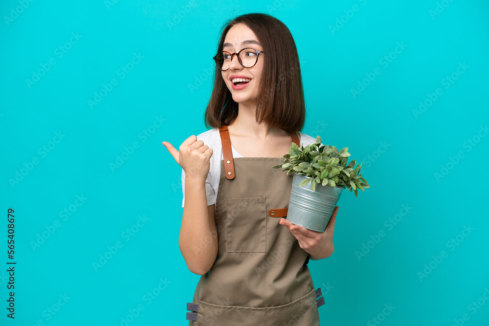 Gardener Ukrainian woman holding a plant isolated on blue background pointing to the side to present a product Gardener Ukrainian woman holding a plant isolated on blue background pointing to the side to present a product
