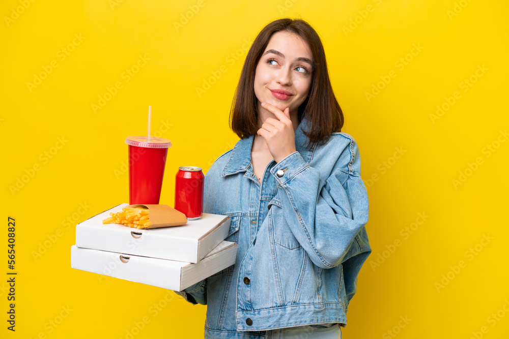 Young Ukrainian woman holding fast food isolated on yellow background and looking up Young Ukrainian woman holding fast food isolated on yellow background and looking up