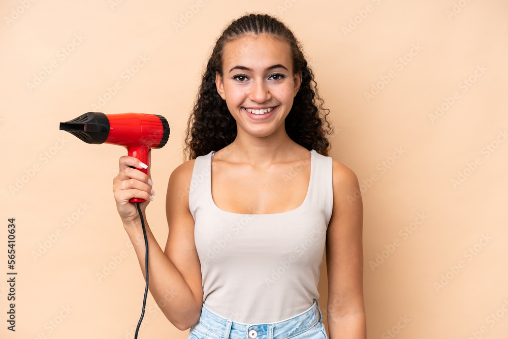 Young woman holding a hairdryer isolated on beige background smiling a lot Young woman holding a hairdryer isolated on beige background smiling a lot
