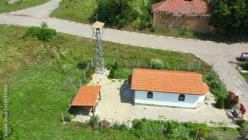 Aerial view of a church with bell tower in the heart of a small balkan village with a white house and a brown roof, a cloudy sky and a forest on the horizon. photo