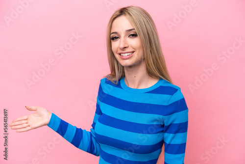 Pretty blonde woman isolated on pink background extending hands to the side for inviting to come © luismolinero