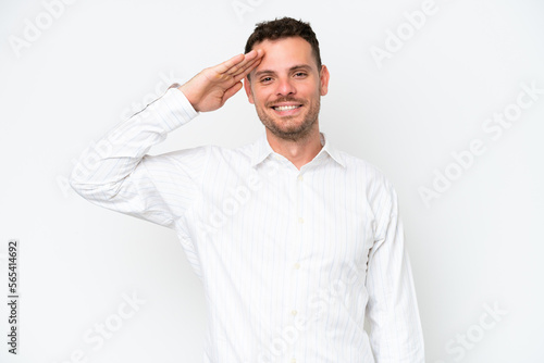 Young caucasian handsome man isolated on white background saluting with hand with happy expression © luismolinero