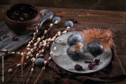 Dyed Easter eggs with marble stone effect painted with natural dye carcade tea from hibiscus flowers, pussy willow branches and feathers on dark wooden background.