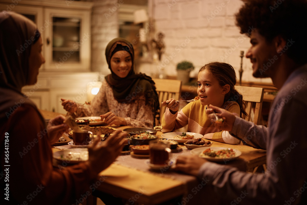 Muslim little girl and her extended family talking while having meal at dining table.