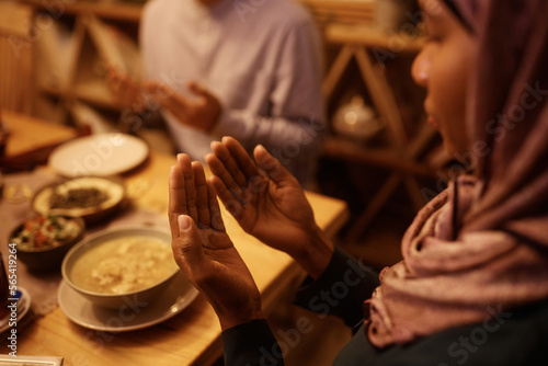 Close up of Middle Eastern woman praying with husband at dining table.