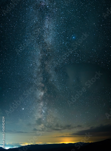 Milky way seen seen from the mountains, rising above urban city lights in a summer night. Astrophotography with stars and constellations. 