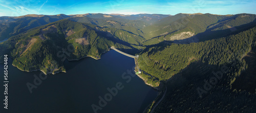 Aerial drone view above Vidra lake. An arched concrete dam holds the water. The dam is built within the wilderness of Lotru Mountains in a narrow valley. Carpathia  Romania.