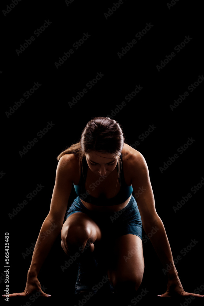 Female runner in low race start position. Girl in sportswear against dark background.. Female runner in low race start position. Girl in sportswear against dark background..