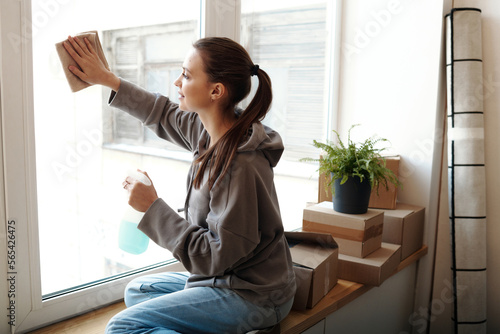 Young woman wiping windows with rag, she putting things in order in her new home