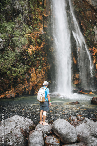 A man with a backpack stands with a backpack near the Grunas waterfall in Albania, at Theth National Park on a hike in Albania.