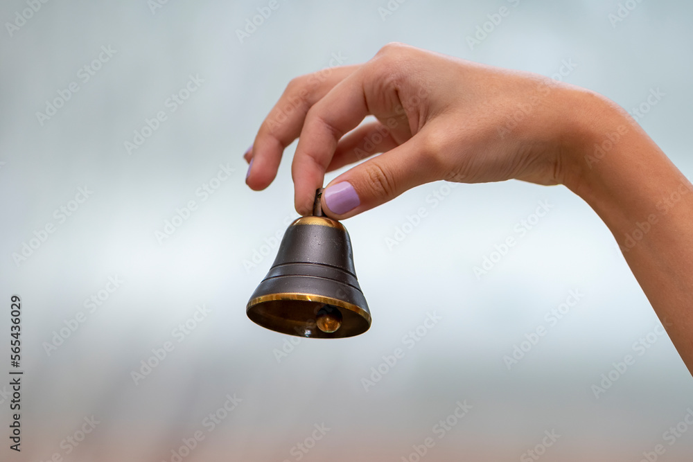 A small bell in the girl's hand on a neutral background, close-up