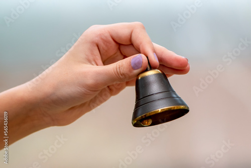 A small bell in the girl's hand on a neutral background, close-up, photo