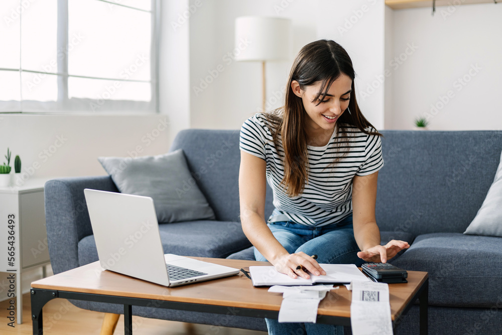 Young woman calculating household tax bills and expenses sitting on sofa at cozy home. Young woman calculating household tax bills and expenses sitting on sofa at cozy home.
