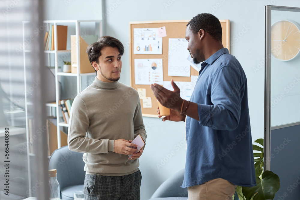 Waist up portrait of two men wearing casual clothes chatting in office setting Waist up portrait of two men wearing casual clothes chatting in office setting