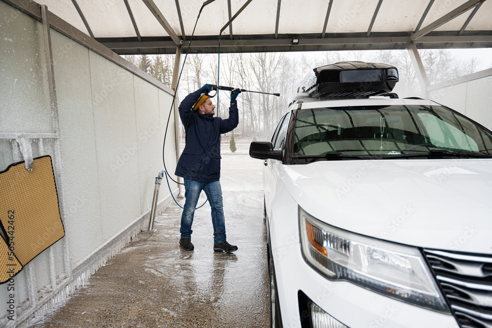 custom made wallpaper toronto digitalMan washing high pressure water american SUV car with roof rack at self service wash in cold weather.