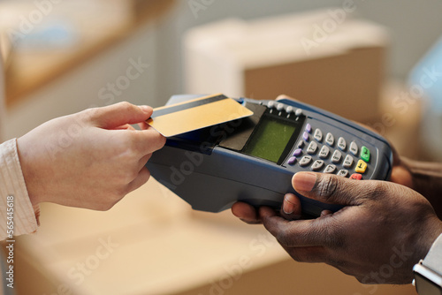 Close-up of young woman using credit card to pay for service during relocation to a new office